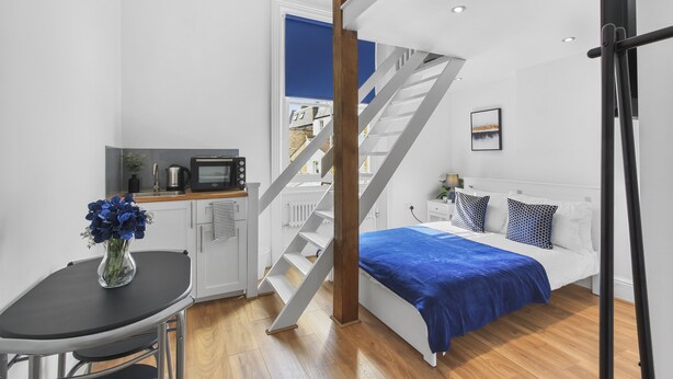 Ein modernes Schlafzimmer mit Bett, Nachttisch und Schreibtisch mit Computer. Eine Treppe führt in einen anderen Raum.