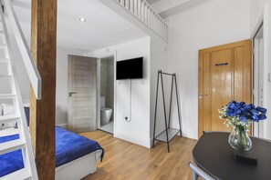 A bedroom with a bed, a television mounted on the wall, a wooden door, and a small table with a vase of flowers. - Our split level Duplex is setup to give you an experience of home away from home (london)