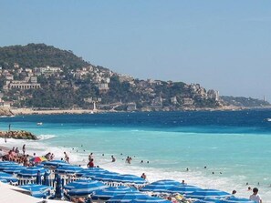 A beach with blue umbrellas and people swimming.