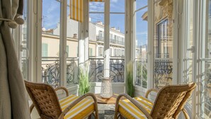 A room with wicker chairs, a table, and a view of buildings through large windows. - Sublime flat, city centre, modern, balconies, air conditioning, refurbished (Nice)