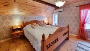 A wooden-framed bed with a white lace bedspread, a nightstand with a lamp, and a window with a red curtain. - Beautiful home in Vedum with kitchen (Vedum)