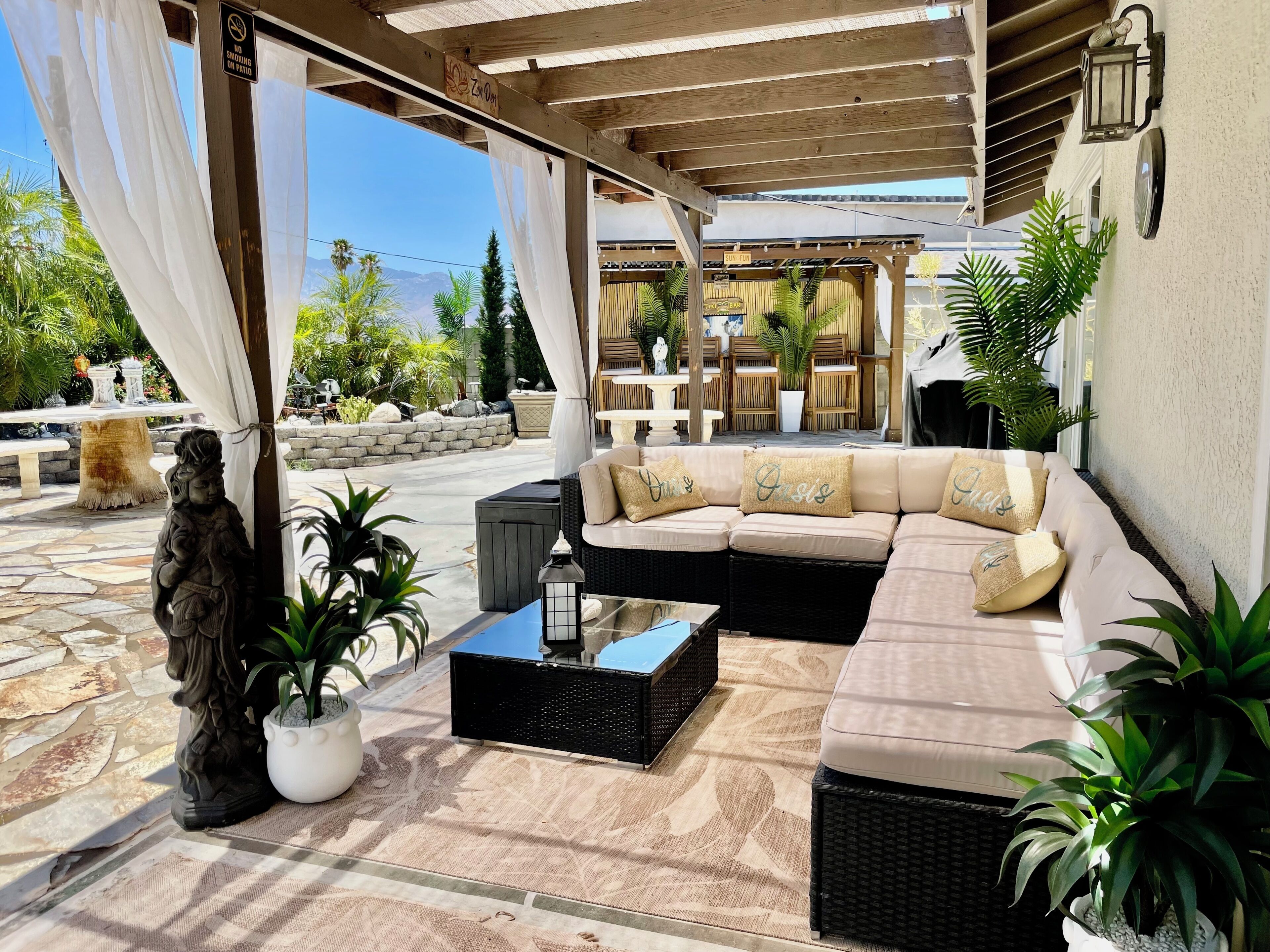 An outdoor seating area with a sofa, cushions, a table, and potted plants.