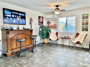 A living room with a wooden cabinet, a TV, a ceiling fan, a large plant, and two chairs.