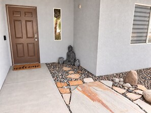 Una entrada de casa con felpudo, una estatua de Buda y un camino de piedra que conduce a la puerta.