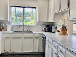 A modern kitchen with a large island, white cabinetry, a built-in sink, and a window overlooking greenery.