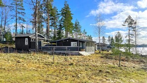 A cabin with a large deck and a covered porch, surrounded by tall trees and a lake. - Beautiful home in Kil with WiFi (Kil)
