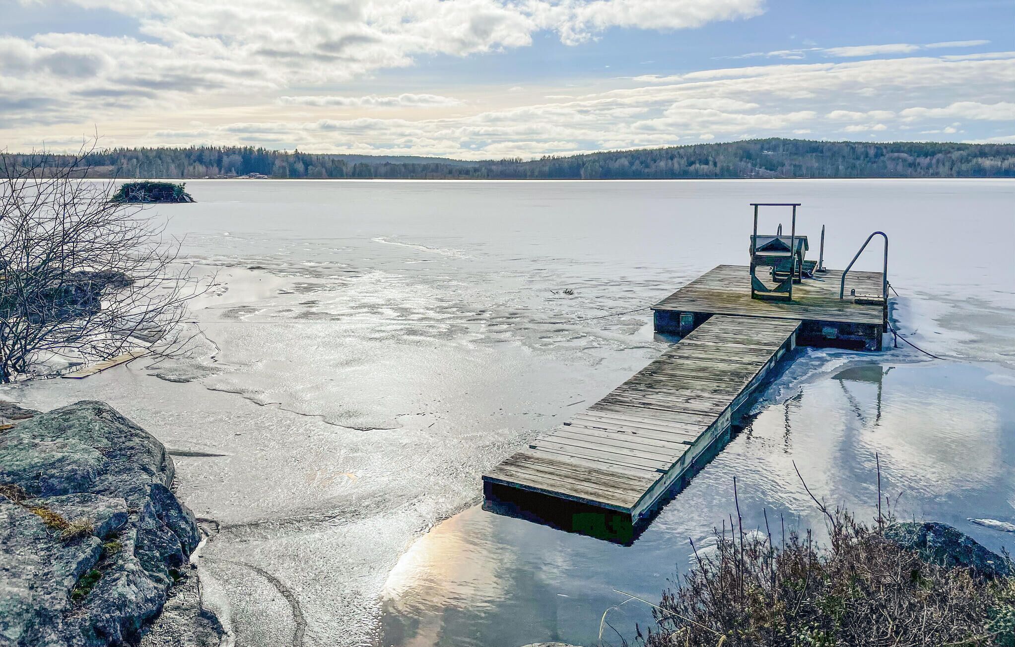 Un muelle de madera que se adentra en un lago congelado, con una pequeña plataforma y zona de estar.