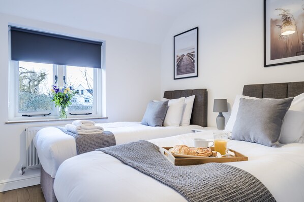 A hotel room with two beds, a window with a view, a framed picture on the wall, and a breakfast tray on the bed.