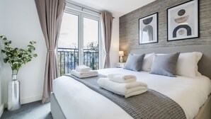 A modern hotel room with a large bed, a view of the city, and abstract art on the wall. - Cozy 3 Bedroom Terrace Cottage in Epsom (Epsom)