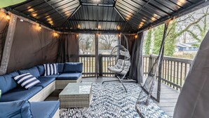 Een overdekt terras met een comfortabele bank, een hangstoel en een vloerkleed met dessin.