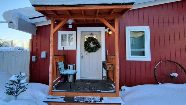 A wooden porch with a snow-covered roof, a door with a wreath, and a small table with chairs. - A Private City, Cabin-feel Studio for 1 Person (Fairbanks)