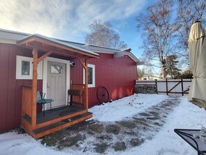 A red building with a porch, a door, and a wheelbarrow.