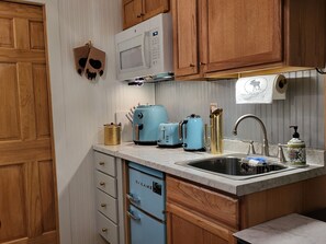 A kitchen with wooden cabinets, a white microwave, a blue toaster, a sink with a soap dispenser, and a dish rack.