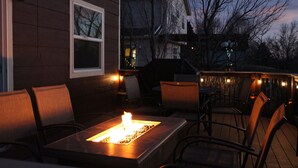 Patio esterno con focolare, sedute e luci decorative a catena.