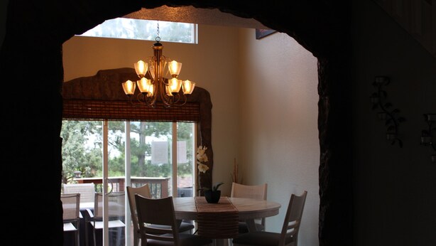 Zona pranzo con tavolo rotondo e sedie, un lampadario e vista su un patio esterno attraverso una porta vetrata.