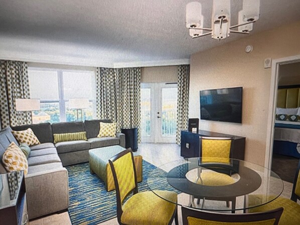 A modern hotel room with a sofa set, a glass coffee table, and a flat-screen TV.