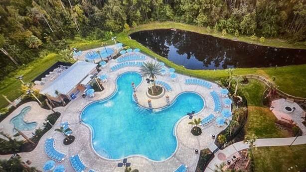 Luchtbeeld van een resort met een groot centraal zwembad, omringd door terrasjes en een klein vijvertje.