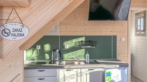 Una kitchenette con un lavamanos, una tetera y una botella de detergente. Hay un cartel que dice 'Zakaz Palenia' y un televisor montado en la pared.