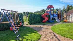 Un parque infantil con un tobogán rojo, estructuras de escalada azules y una casita de juegos con techo rojo.