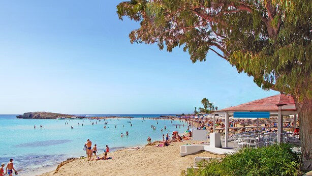 Een strand met een paviljoen, mensen die zonnebaden en een helderblauwe lucht.