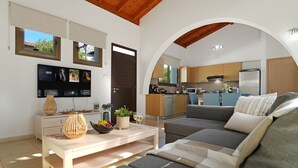Een moderne woonkamer met een bank, salontafel en televisie. Een keuken is zichtbaar door een boog.