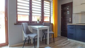 A modern kitchen with a dining area, featuring a table and chairs, a window with blinds, and a door with cabinets. - 2 bedroom amazing home in Mielno (Mielno)