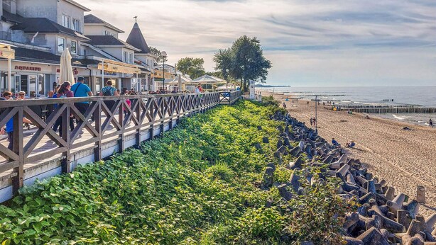 A coastal walkway with a wooden railing, a beach in the background, and a row of buildings with visible signage. - 2 bedroom amazing home in Mielno (Mielno)