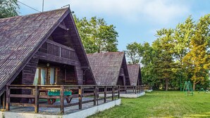 A row of wooden cabins with pitched roofs, a wooden deck in front, and a grassy area with trees. - 2 bedroom amazing home in Mielno (Mielno)