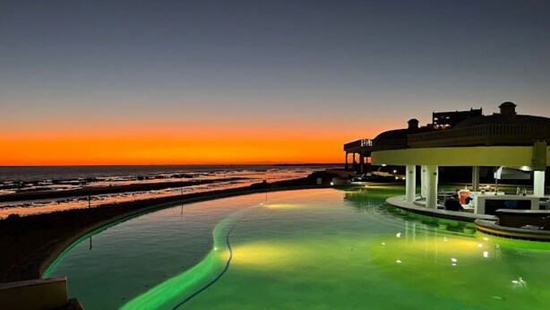 A swimming pool with a curved edge, a building with a flat roof, and a sunset over the ocean. -  Welcome to Rocky Point Mexico. Enjoy the most beautiful Beach in Rocky Point . (Puerto Peñasco)
