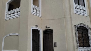 Un bâtiment à la façade beige, aux ornements blancs et doté d’un escalier menant à une entrée de couleur sombre.