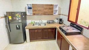 Une cuisine compacte équipée d’un réfrigérateur, d’un évier à deux bacs, de meubles de rangement en bois et d’une cuisinière à gaz.