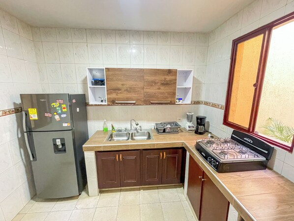 A compact kitchen with a refrigerator, double sink, wooden cabinets, and a gas stove.