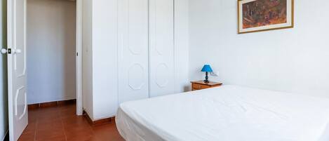 A bedroom with a bed, a nightstand with a lamp, a door, and a painting on the wall.