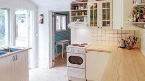 Una cocina con armarios blancos, una estufa y un lavamanos. Hay una ventana y una puerta que da a otra habitación.