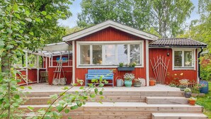 Una casa roja de madera con un ventanal grande, un banco azul y una escalera de madera que lleva a la puerta principal.