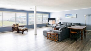A spacious living room with a grey sectional sofa, a wooden coffee table, and a chair. Large windows provide a view of the outside. - Island Oasis with a view (Dauphin Island)