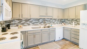 A modern kitchen with grey cabinets, a white countertop, a tiled backsplash, and a built-in dishwasher. - Island Oasis with a view (Dauphin Island)