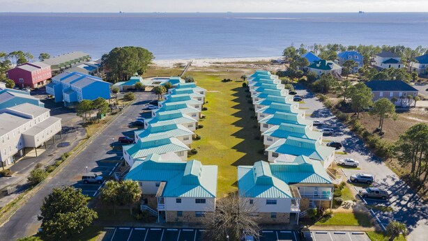 A coastal hotel with a row of blue-roofed buildings, a parking lot, and a beach view. - Island Oasis with a view (Dauphin Island)