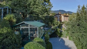 Ein Wintergarten mit Metallveranda, umgeben von üppiger Bepflanzung und einem Kiesweg, der zu einem traditionellen Backsteinhaus führt.