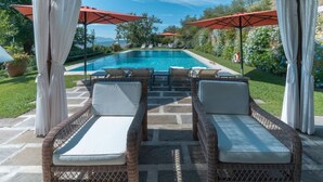 Ein Poolbereich mit Korlounge-Stühlen, einer Steinterrasse und roten Sonnenschirmen.