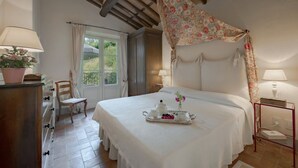 Ein Schlafzimmer mit einem Bett, einem Schminktisch, einem Stuhl, einem Fenster und einem Nachttisch mit Lampe.