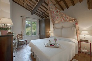 Un dormitorio con cama, cómoda, silla, ventana y mesita de noche con lámpara.