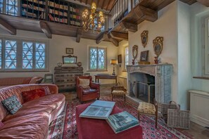 Amplia sala de estar con chimenea, estanterías, un sofá rojo y un tapete estampado.