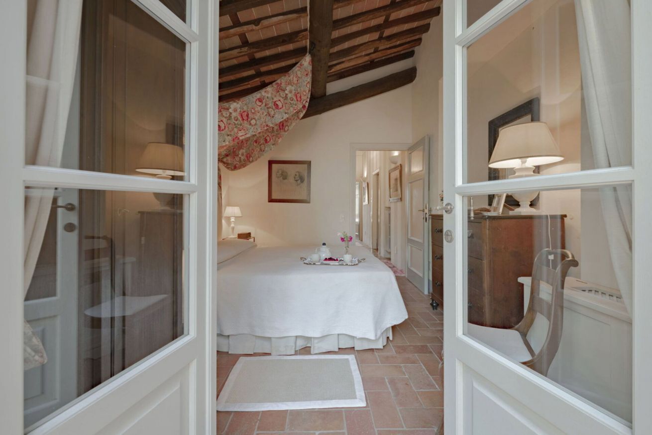 A room with a bed, a table with a tray, a chair, and a window with curtains.