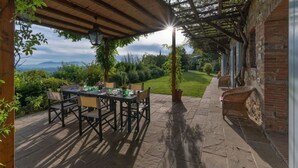 Eine Terrasse im Freien mit Tisch und Stühlen, einer Ziegelwand und Blick auf die Landschaft.