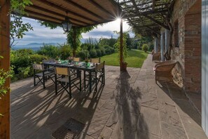 Un patio exterior con una mesa y sillas, un muro de ladrillo y vistas del paisaje.