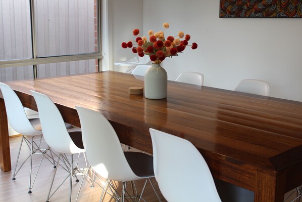 A dining table with a vase of flowers, white chairs, and a wooden floor.