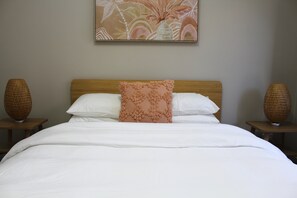 A neatly made bed with white linens, a wooden headboard, and a decorative pillow. There are two bedside tables with woven lamps. - Sunbury on the Park - netflix, table tennis (Sunbury)