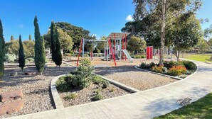 A playground with a slide and climbing structures, surrounded by landscaped areas with shrubs and trees. - Sunbury on the Park - netflix, table tennis (Sunbury)