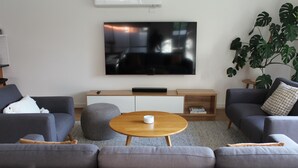 A modern living room with a flat-screen TV, grey sofas, a wooden coffee table, and a large plant. - Sunbury on the Park - netflix, table tennis (Sunbury)